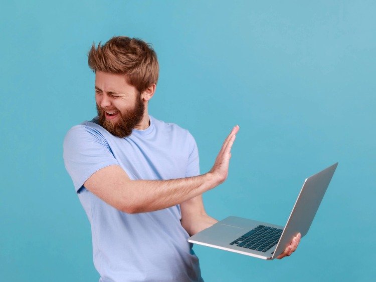 Junger Mensch wendet sich ab von seinem Laptop und streckt die Hand abwehrend aus