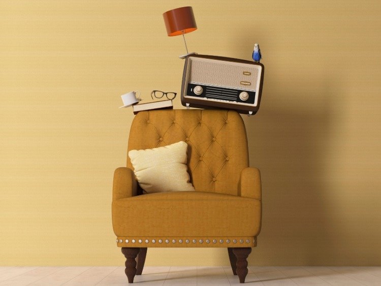 Ein gemütlicher Sessel. Auf der Rückenlehne stapeln sich Radio, Brille, Bücher und eine Kaffeetasse