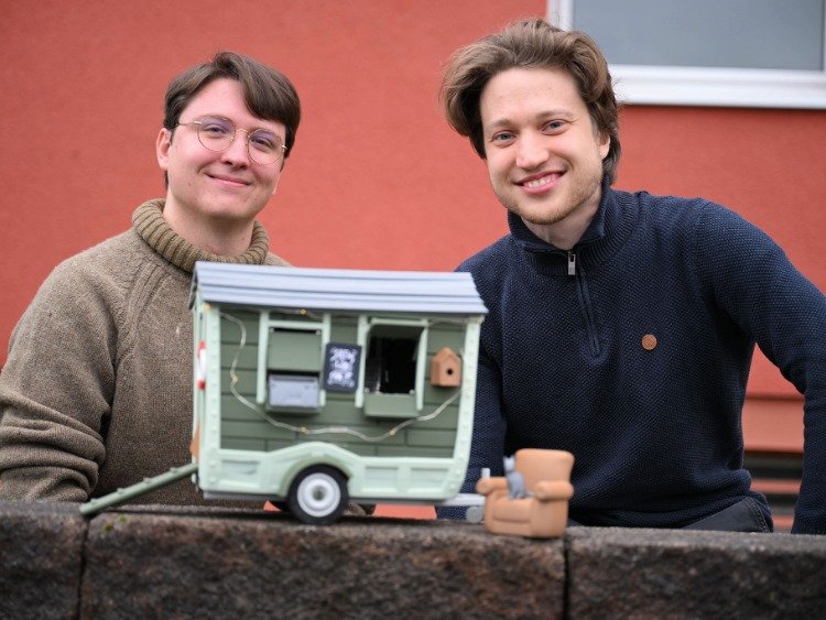 Auf dem Foto sind die Computerspieleentwickler David Zapfe-Wildemann und Raven Rusch zu sehen. Der kleine Bauwagen im Vordergrund steht symbolisch für das Spiel "Tiny Bookshop"