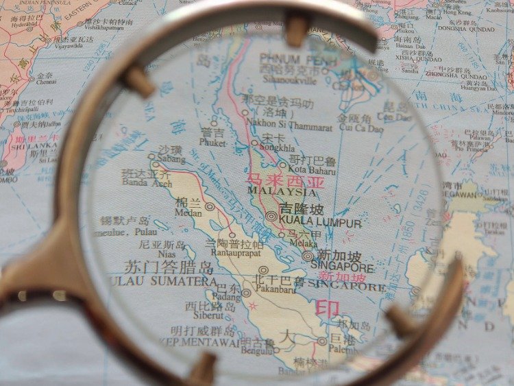 Eine Lupe vergrößert den Ausschnitt eine rLandkarte, auf der die Straße von Malakka zu sehen ist. Sie liegt zwischen der indonesischen Insel Sumatra im Westen sowie der Malaiischen Halbinsel