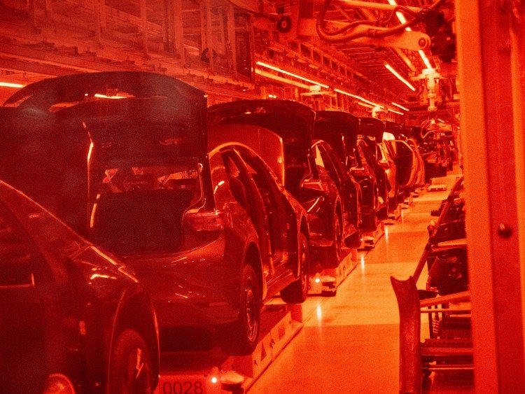 VW in Zwickau: zu sehen sind hintereinander stehende Autos zur Fertigung, die Halle ist in ein rotes Licht getaucht
