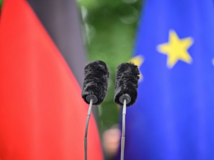 Zwei Mikrofone im Vordergrund. Im Hintergrund die Deutschland-Fahne und die der Europäischen Union