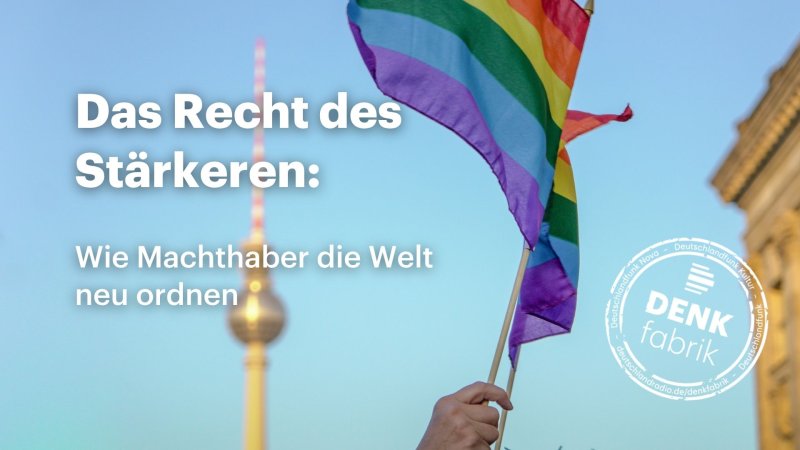 Eine Regenbogenflagge wird in den Himmel gestreckt. Im Hintergrund ist die Kuppel des Berliner Fernsehturms zu sehen.