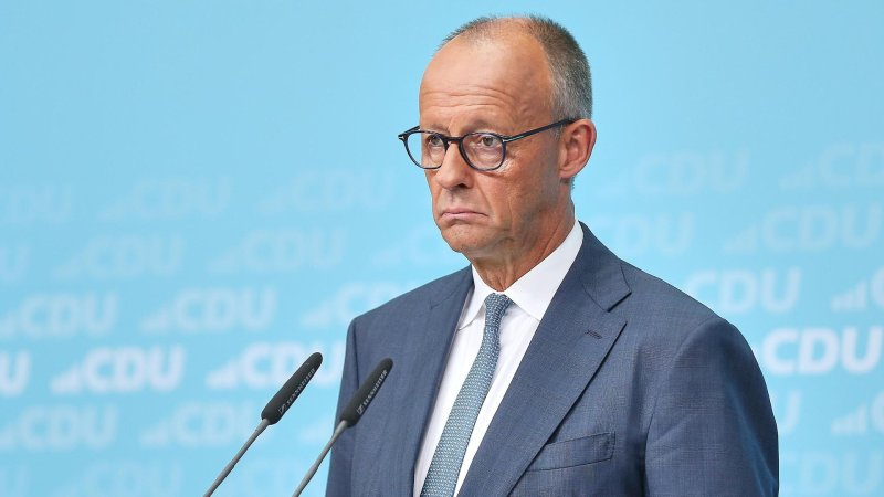Bundeskanzler Friedrich Merz steht im Anzug an einem Rednerpult mit zwei Mikrofonen vor einem blauen Hintergrund mit CDU-Schriftzügen. Er trägt eine Brille und blickt sehr ernst nach vorn.