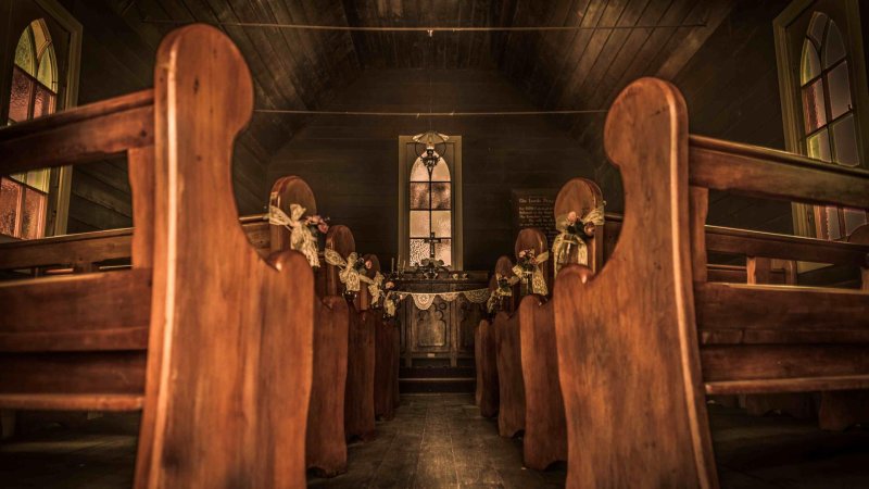 Blick entlang des leeren Gangs einer hölzernen Siedlerkirche zum Altar.