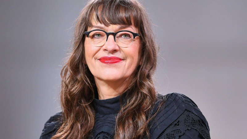 Eine Frau mit Brille vor grauem Hintergrund.