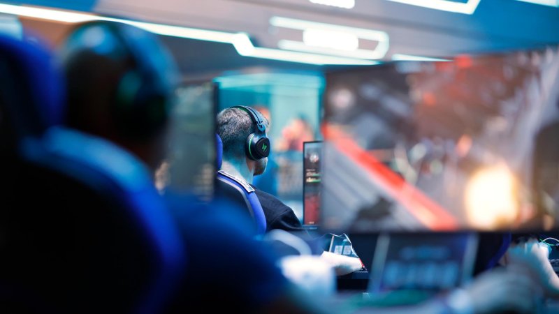 Menschen mit Kopfhörern sitzen vor Bildschirmen und spielen Games auf der Gamescom 2025 in Köln.  