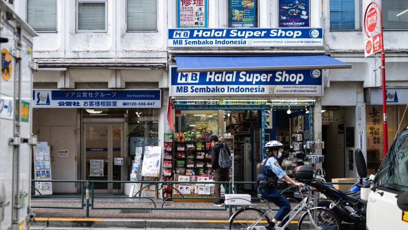 Ein Polizist fährt auf dem Fahrrad im Tokioter Stadtteil Okubo eine Straße entlang, im Hintergrund ein Geschäft, das"Halal Super Shop" heißt. 