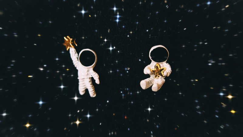 Zwei kleine Astronauten fliegen durchs Weltall, umringt von Sternen. 