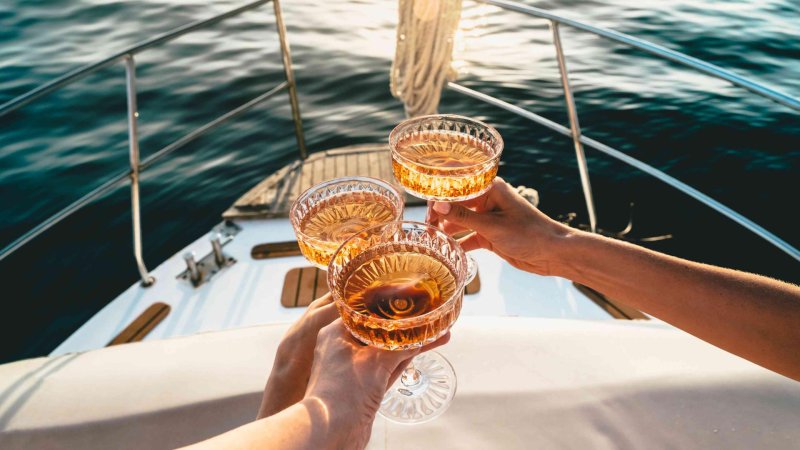 Auf dem Deck eines fahrenden Schiffes wird mit drei Champagnerschalen angestoßen.