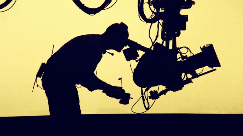 Silhouette eines Kameramanns vor gelbem Hintergrund 