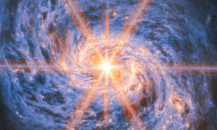 Eine Galaxie mit blau leuchtenden Spiralarmen. Im
orangefarbenen sehr hellen Zentrum steht ein Objekt, von dem acht Strahlen
ausgehen.