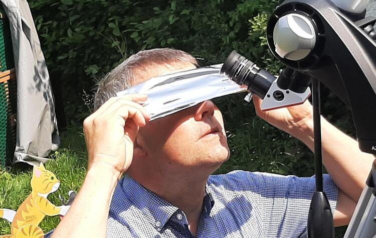 Eine männliche Person hält einen dicken Streifen aus silbrig glänzender Folie vor die Augen und blickt an den Himmel.