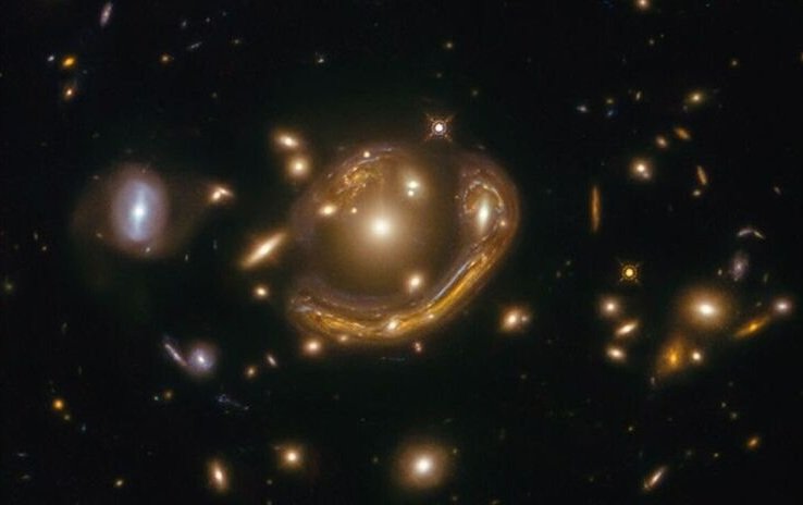 Mitten in einem dunklen Sternfeld befindet sich eine etwas diffuse Galaxie. Fast halb um sie herum windet sich ein stark verformtes Bild einer fernen Galaxie. Dieses Objekt ist auch links oberhalb der diffusen Galaxie zu sehen.