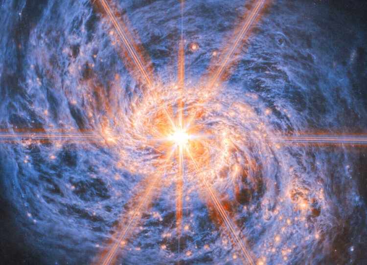 Vor dunklem Hintergrund steht eine Galaxie aus gelb und blau leuchtenden Wolken, die eine große Spiralstruktur bilden. Aus dem hellen gelben Zentrum erstrecken sich acht Lichtstrahlen bis an den Bildrand.
